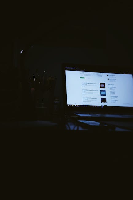 Low light ambiance of a laptop screen glowing in a dark, quiet workspace.